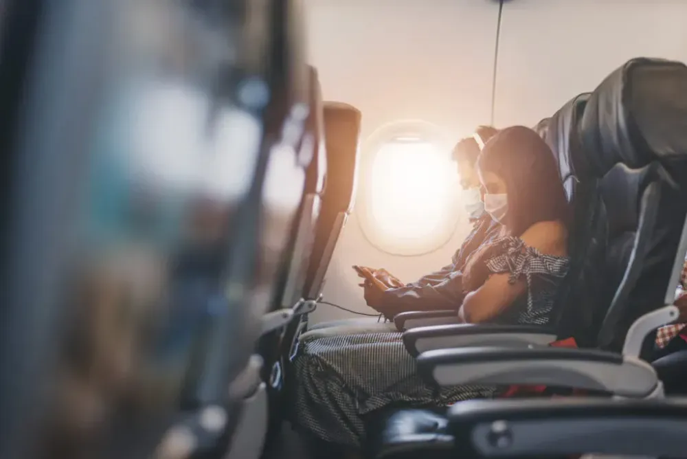 Two passengers on airplane wearing medical face masks as sun comes in through plane window 